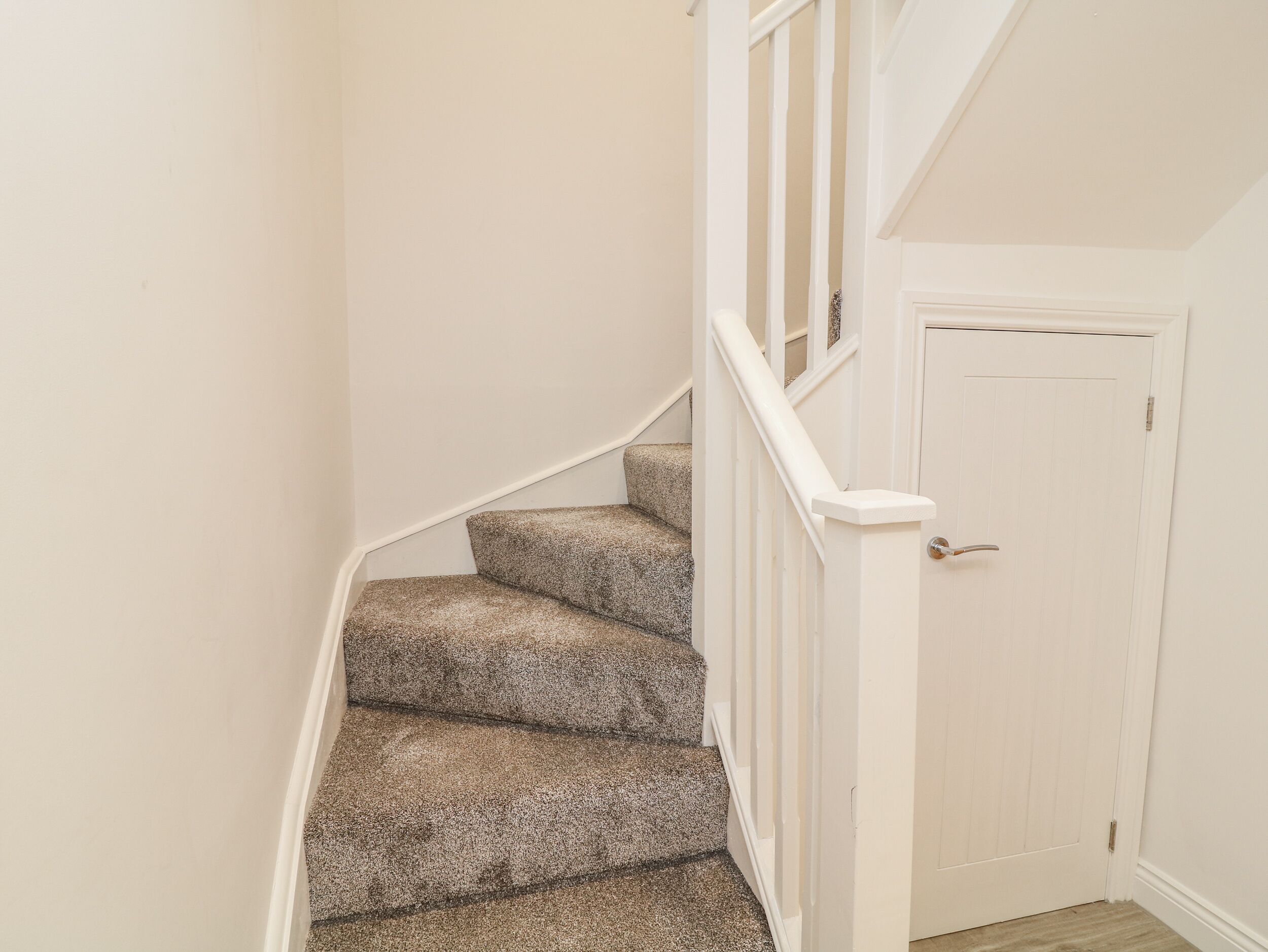 A staircase with carpeted steps and white railings leading to a white door.