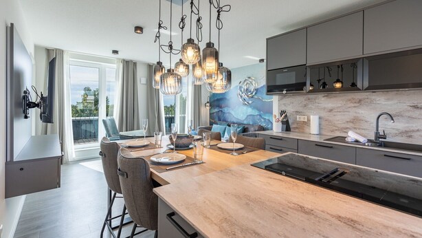 A modern kitchen with a central island, pendant lighting, and a view of the outdoors. - Luxusapartement mit Meerblick (Nordstrand)