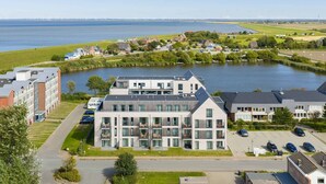 A modern building with multiple floors, large windows, and a parking area with cars. - Luxusapartement mit Meerblick (Nordstrand)