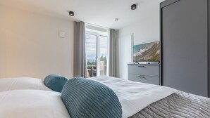 A hotel room with a large bed, a television on a stand, and a balcony with a view of the outdoors. - Luxusapartement mit Meerblick (Nordstrand)