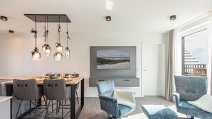 A modern dining area with a wooden table, grey upholstered chairs, and hanging pendant lights. - Luxusapartement mit Meerblick (Nordstrand)