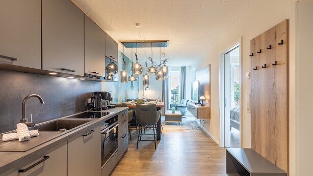 A modern kitchen with a central island, pendant lights, and a view to the living area. - Luxusfewo auf Nordstrand am Meer (Nordstrand)