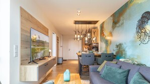 A modern living room with a large flat-screen TV, a grey sofa, and a wooden coffee table. - Luxusfewo auf Nordstrand am Meer (Nordstrand)