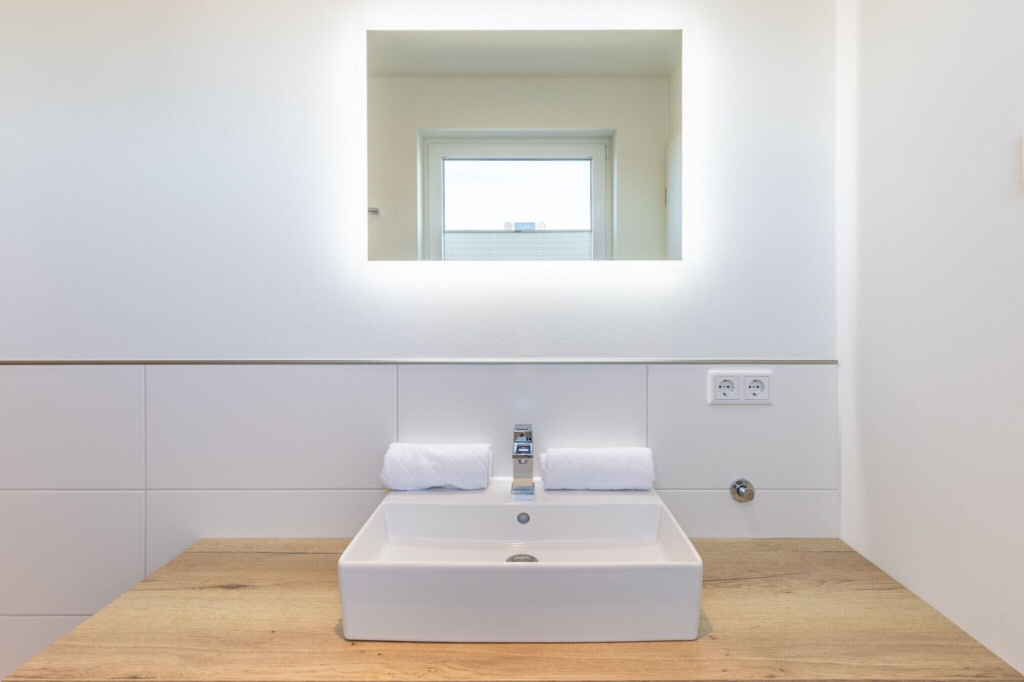 A modern bathroom with a rectangular sink, a mirror above it, and a window with blinds.