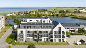 Ein modernes, mehrstöckiges Hotel mit Balkonen, einem Parkplatz und Blick auf einen See und die umliegende Landschaft.