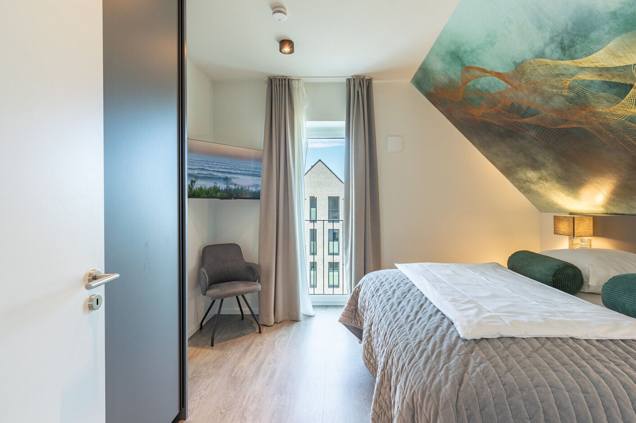 Een moderne hotelkamer met een bed, een stoel, een schilderij en uitzicht op een gebouw.