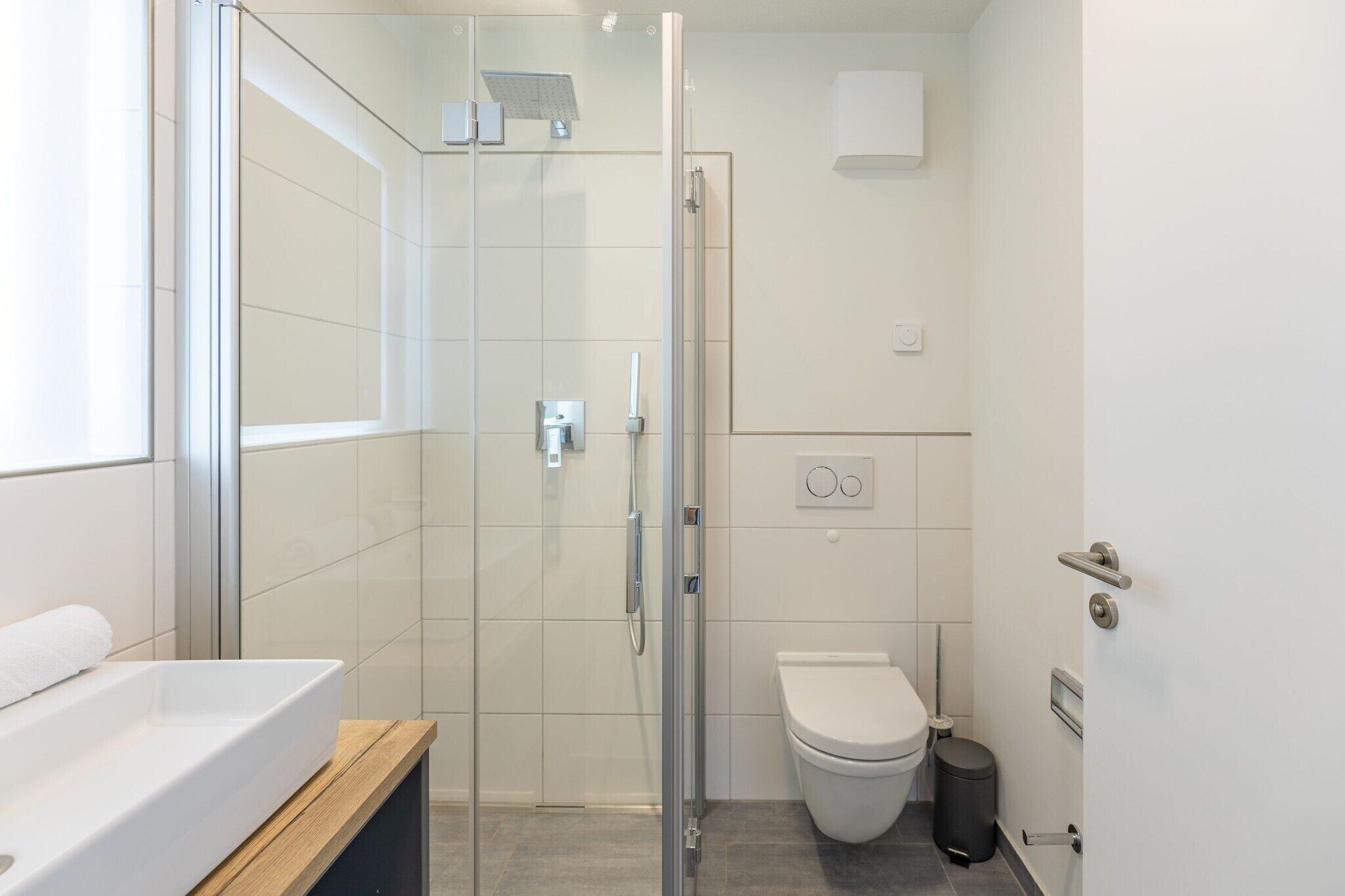 Een moderne badkamer met een glazen douchecabine, een wit toilet en een wastafel met een houten aanrechtblad.