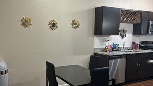 A modern kitchen with dark cabinets, a granite countertop, and a dining area with a black table and chairs. - Charming 2BR/2BA Bed — Cozy, Quiet & Welcoming (McDonough)