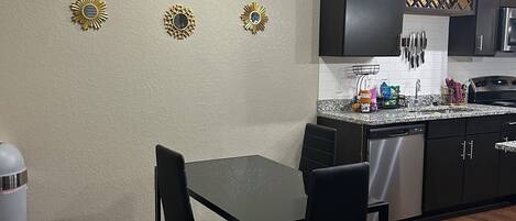 A modern kitchen with dark cabinets, a granite countertop, and a dining area with a black table and chairs.