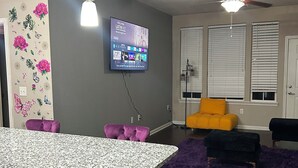 A modern living room with a kitchen island, a ceiling fan, and a flat-screen TV mounted on the wall. - Charming 2BR/2BA Bed — Cozy, Quiet & Welcoming (McDonough)