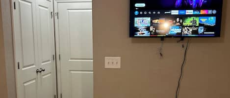 Une pièce dotée d’un téléviseur à écran plat fixé au mur, qui diffuse différents services de streaming. Les portes sont blanches et le sol est recouvert d’une moquette.