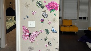 A room with a floral wallpaper, a bed, a yellow chair, and a window with blinds. - Charming 2BR/2BA Bed — Cozy, Quiet & Welcoming (McDonough)