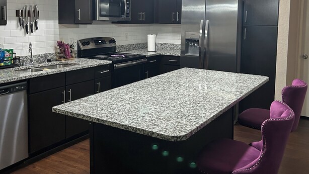 A modern kitchen with dark cabinets, a granite countertop, stainless steel appliances, and pendant lighting. - Charming 2BR/2BA Bed — Cozy, Quiet & Welcoming (McDonough)
