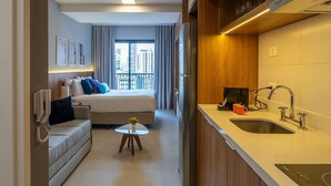 A compact hotel room with a kitchenette, a bed with a view, a small seating area, and a phone on the wall. - Upper West Perdizes by Xtay (São Paulo)