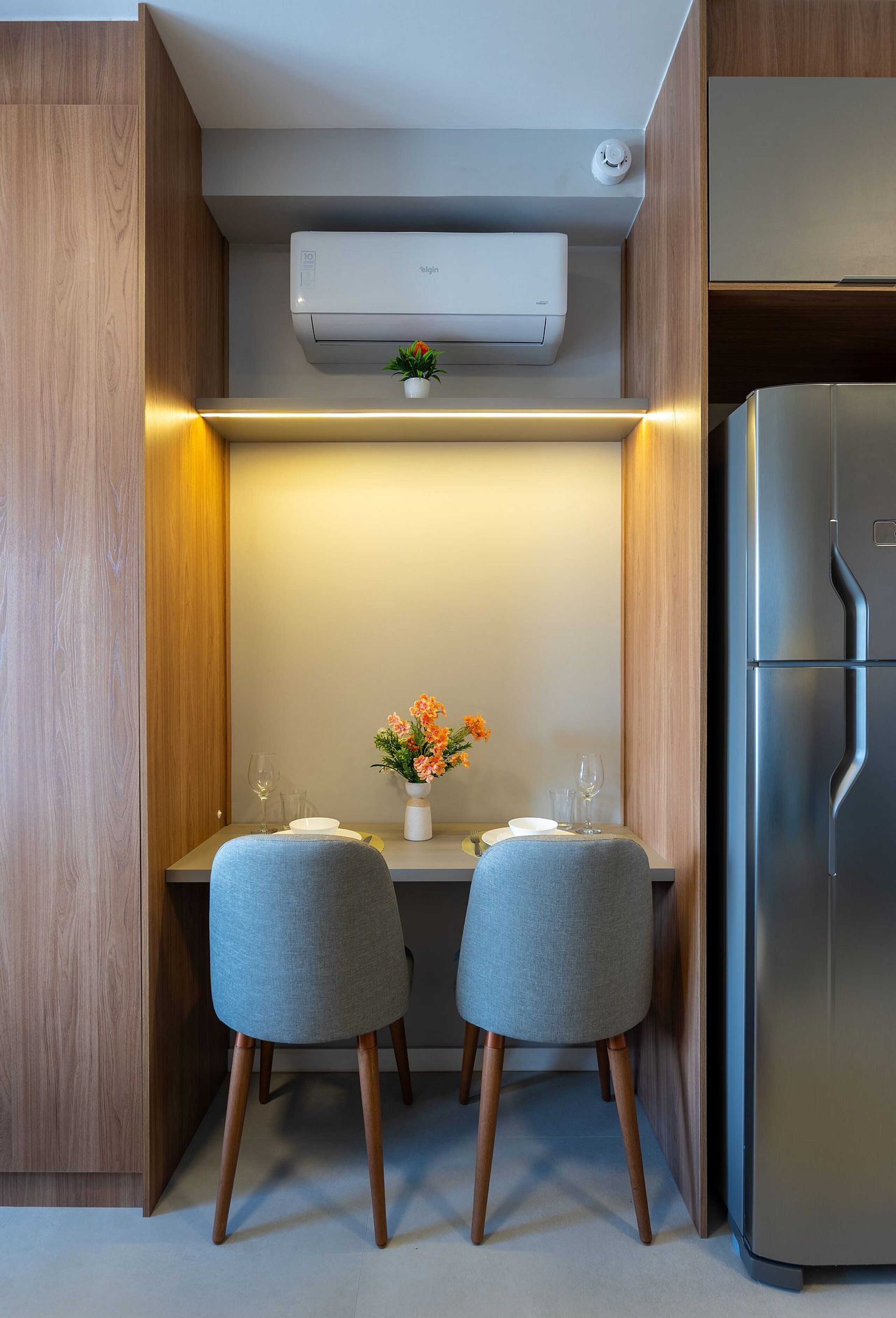 A compact kitchen with a built-in air conditioner, a stainless steel refrigerator, and a small table with two chairs.