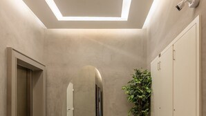 A modern hallway with a ceiling light, a security camera, a potted plant, and a mirrored wall. - Upper West Perdizes by Xtay (São Paulo)
