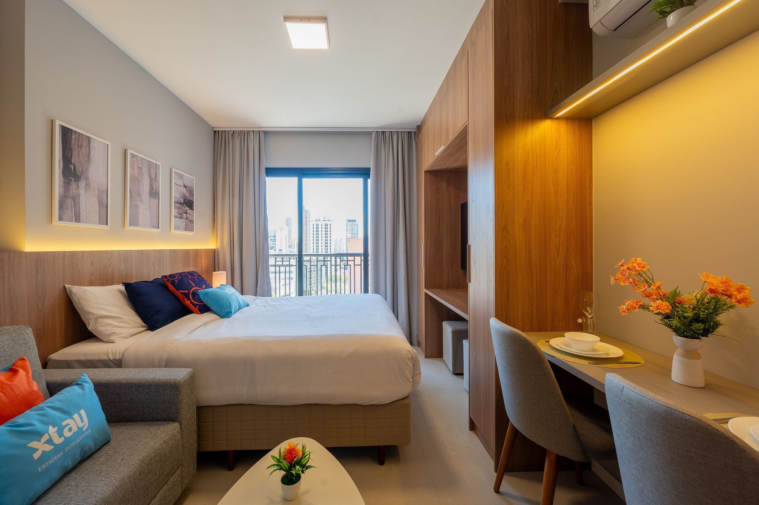 A modern hotel room with a large bed, a desk, and a view of the city.