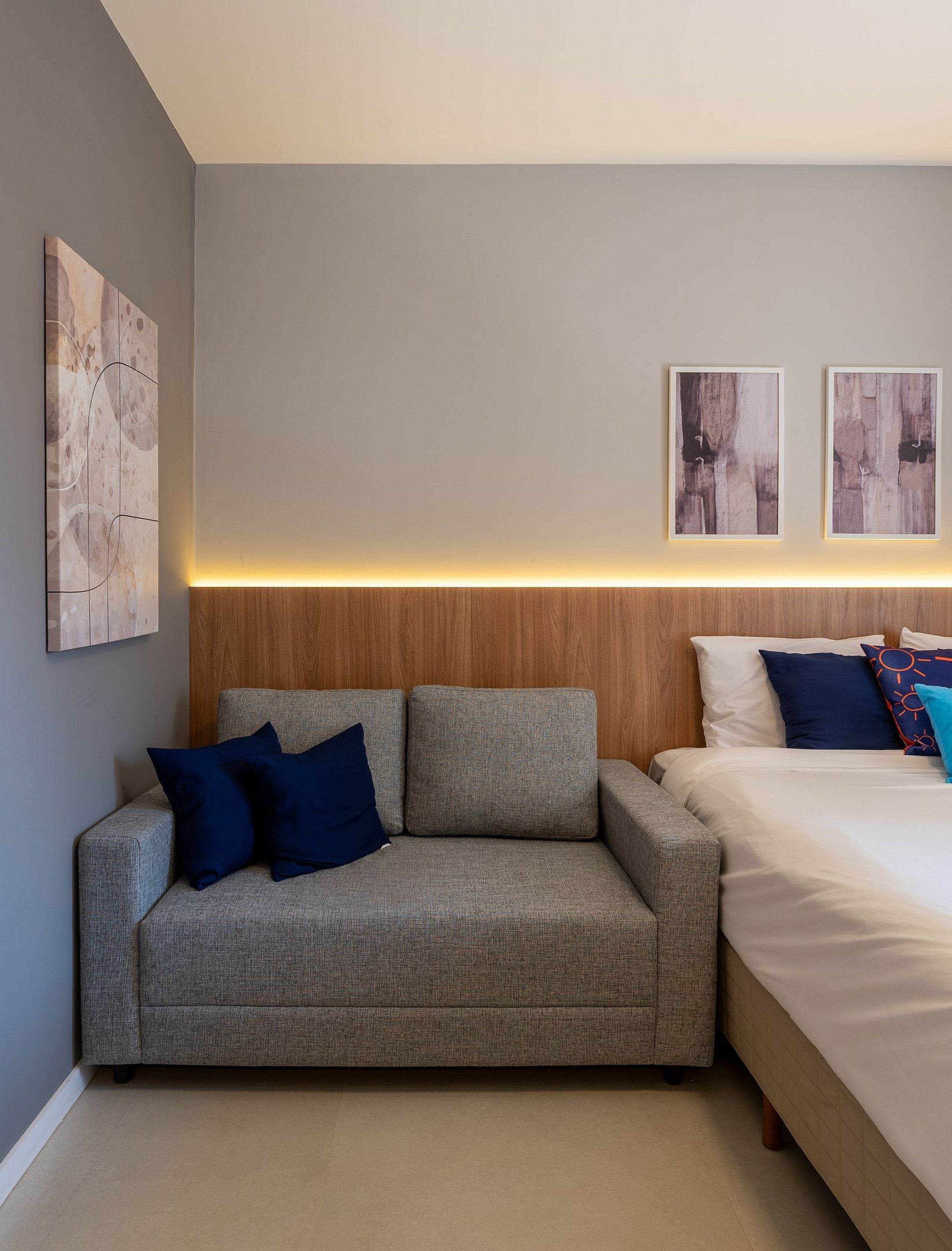 A modern bedroom with a grey sofa, a wooden headboard, and a bed with white and blue bedding.