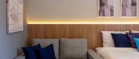 A modern bedroom with a grey sofa, a wooden headboard, and a bed with white and blue bedding.