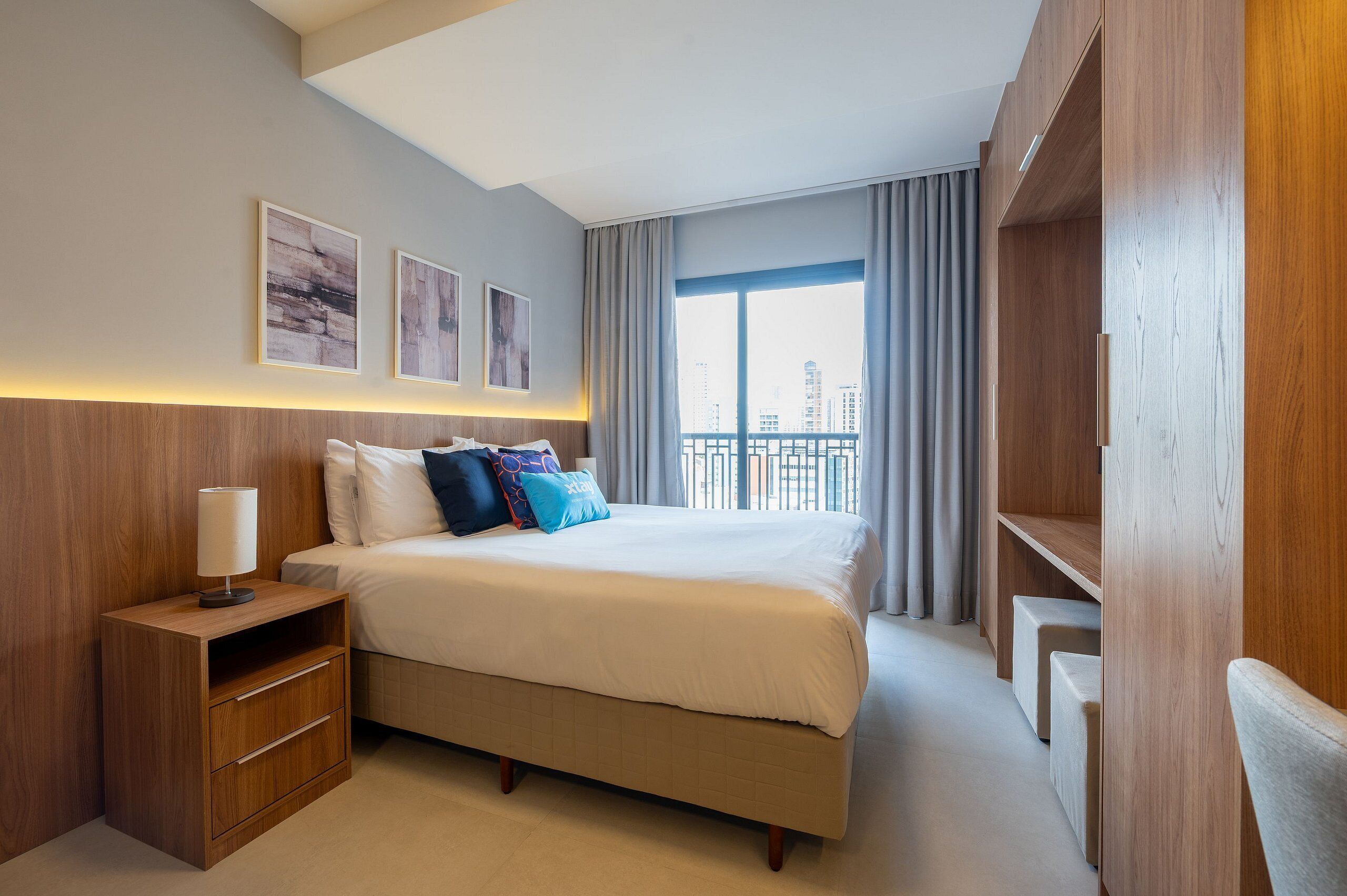 A modern hotel room with a large bed, a nightstand, and a wardrobe.