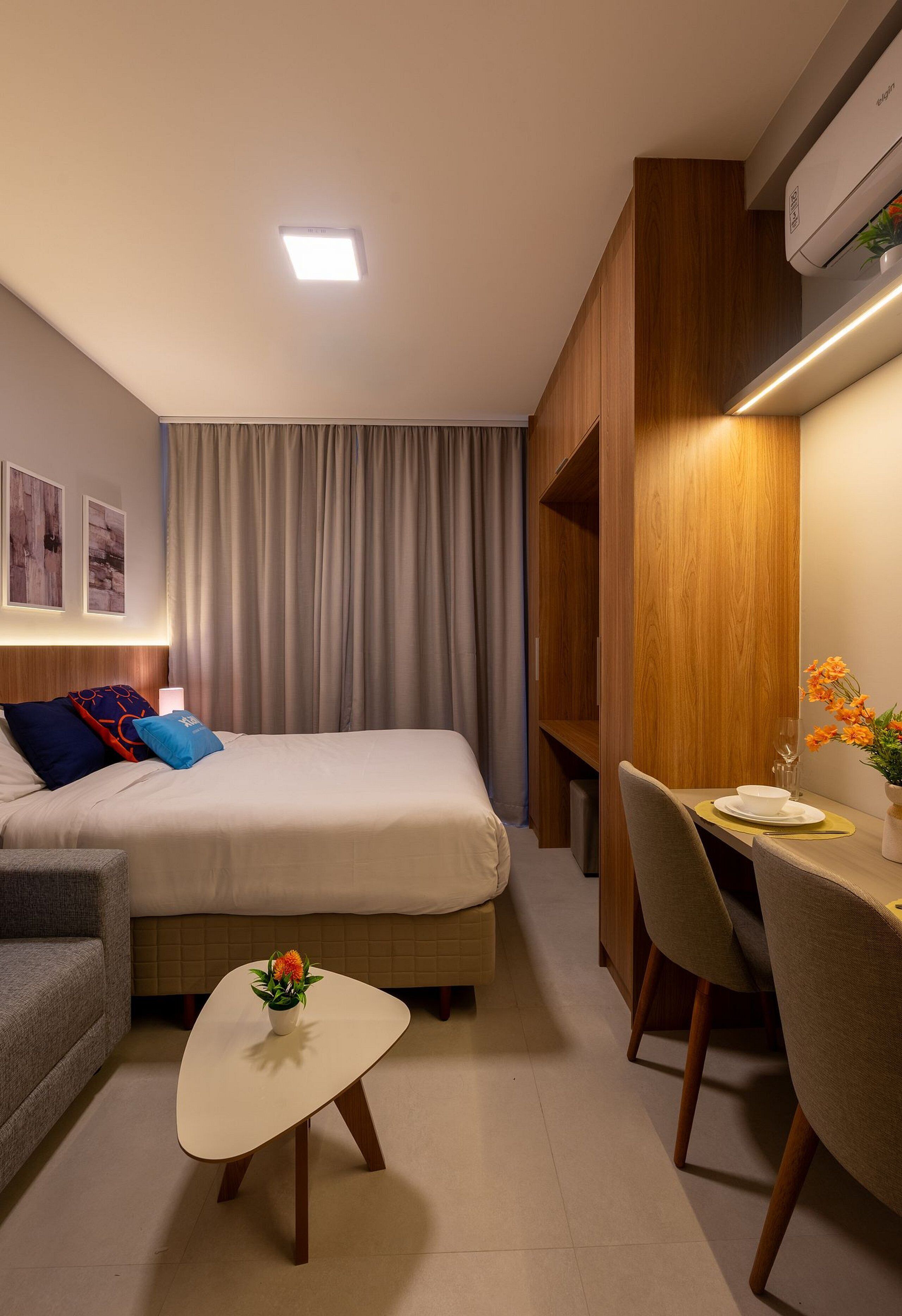 A modern hotel room with a bed, a desk, and a small table with a flower.