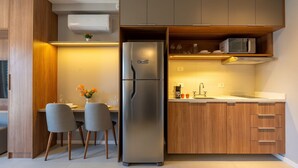 A modern kitchen with a built-in refrigerator, wooden cabinets, and a dining area with two chairs and a table. - Upper West Perdizes by Xtay (São Paulo)