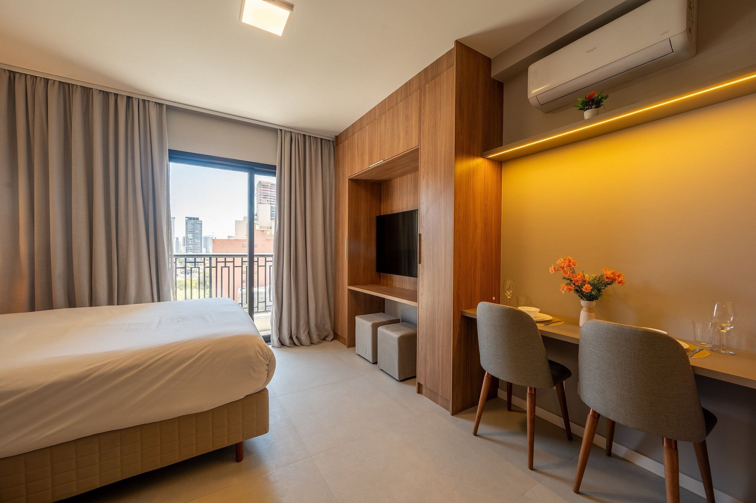 A hotel room with a bed, a desk with two chairs, a TV, and a small plant.