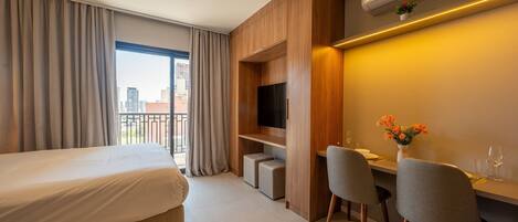 A hotel room with a bed, a desk with two chairs, a TV, and a small plant.