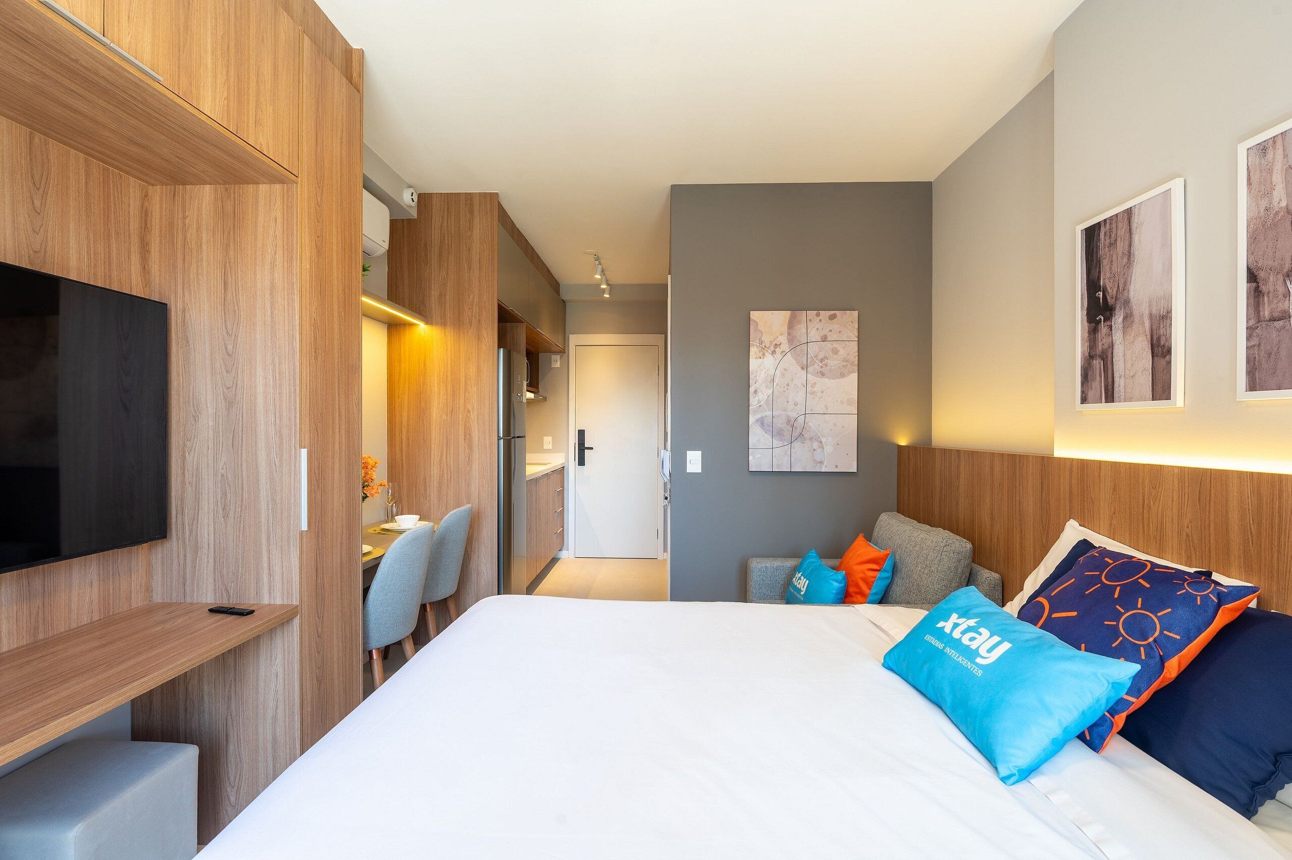A modern hotel room with a large bed, a TV, a desk, and a dining area.
