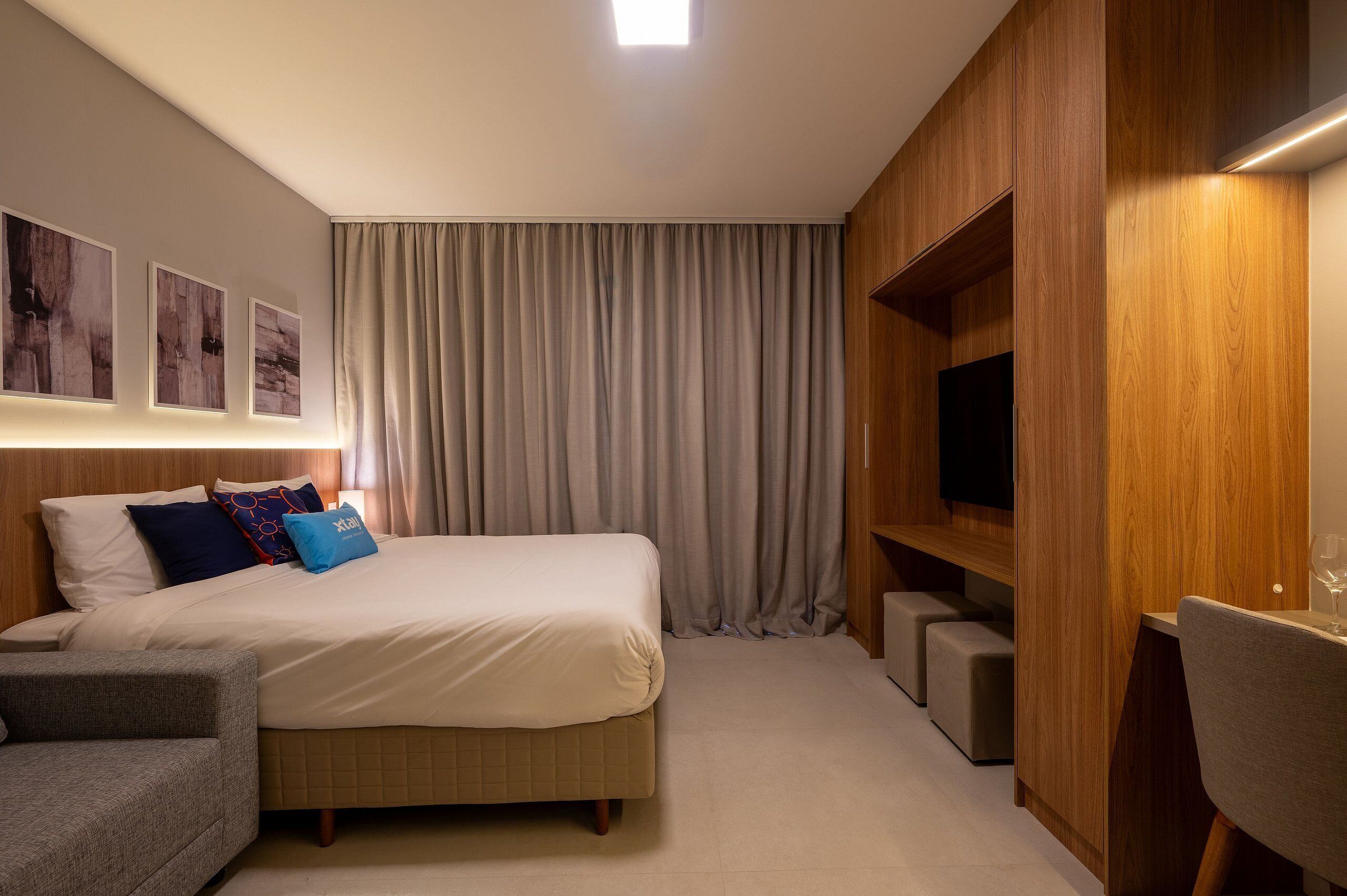 A hotel room with a bed, a TV, a seating area, and artwork on the wall.