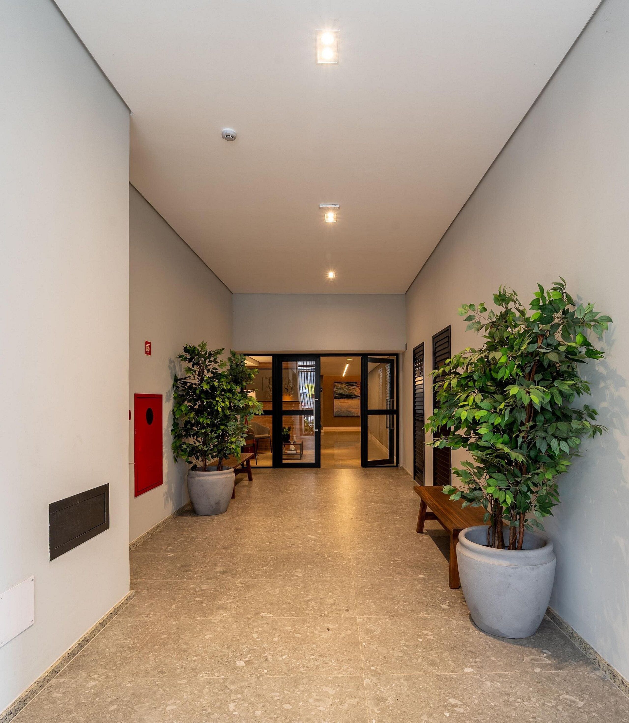 A hallway with a tiled floor, potted plants, a bench, and a door leading to a room.