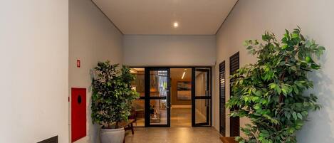 A hallway with a tiled floor, potted plants, a bench, and a door leading to a room.