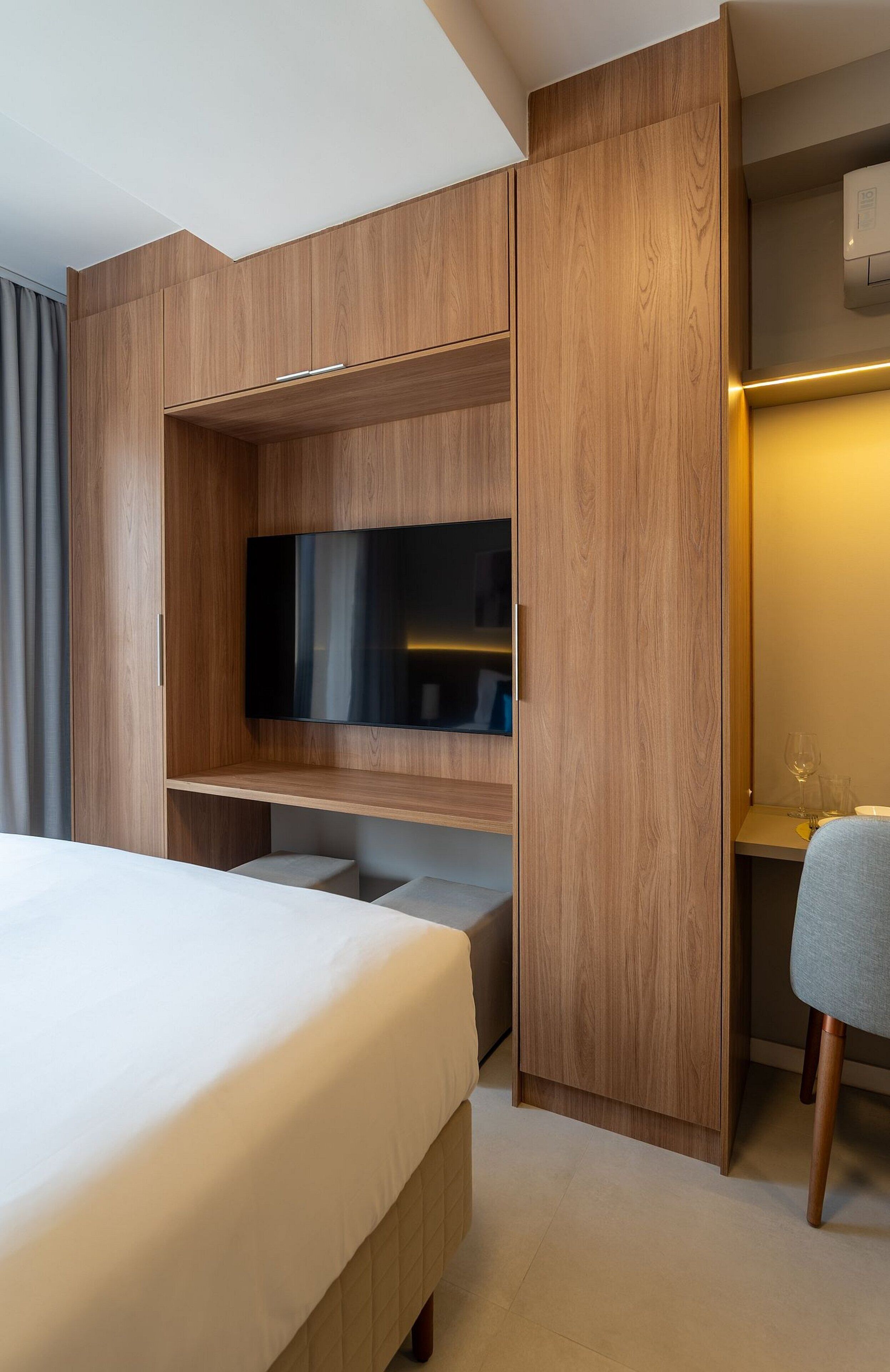 Una habitación de hotel moderna con una cama grande, un televisor de pantalla plana montado en una pared de madera y una pequeña zona de estar con una mesa y sillas.