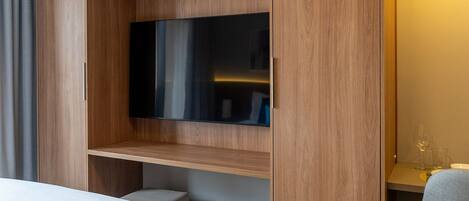 Una habitación de hotel moderna con una cama grande, un televisor de pantalla plana montado en una pared de madera y una pequeña zona de estar con una mesa y sillas.