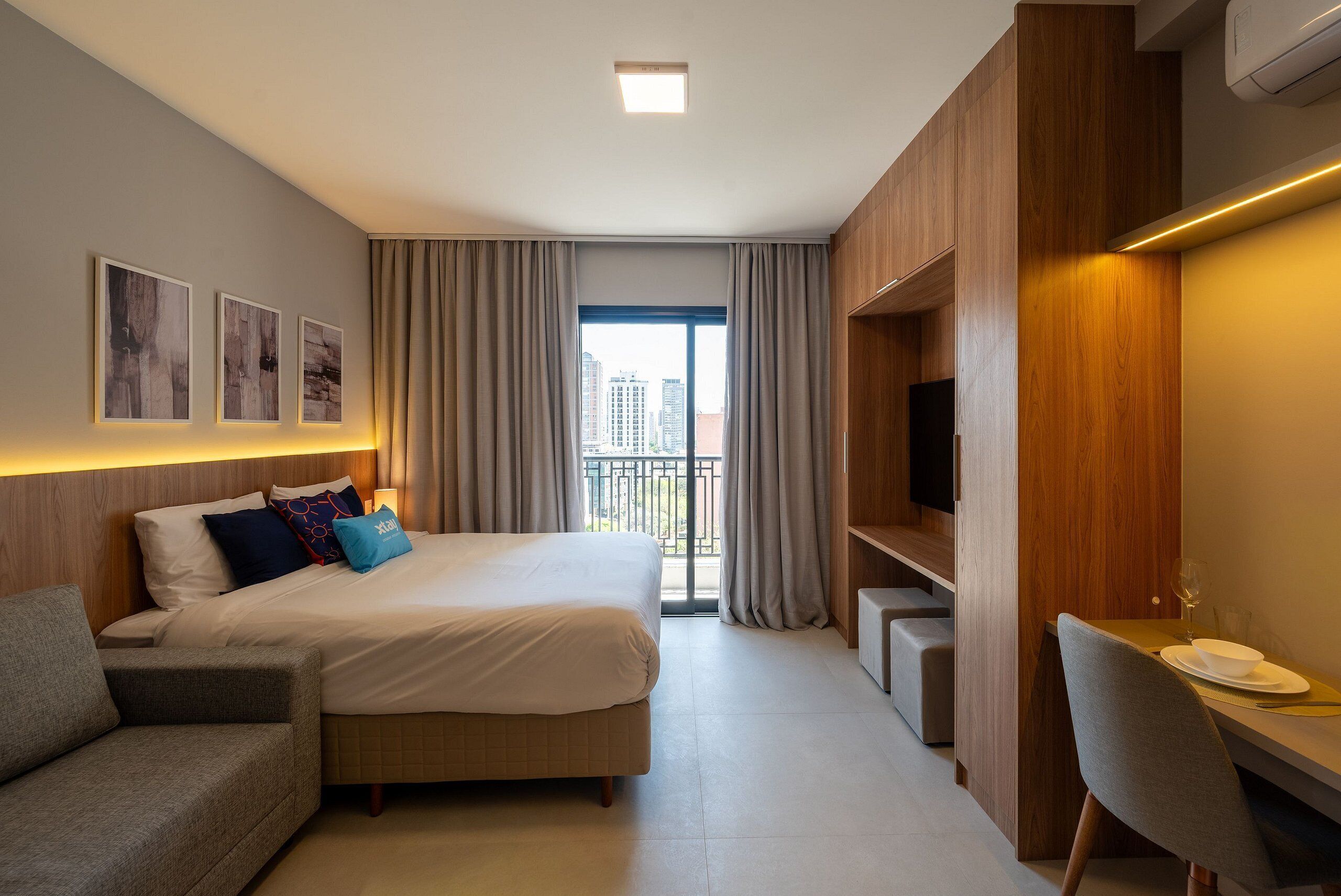 Ein Hotelzimmer mit Bett, Sofa, Schreibtisch mit Stuhl, Fernseher und einem Balkon mit Vorhängen.