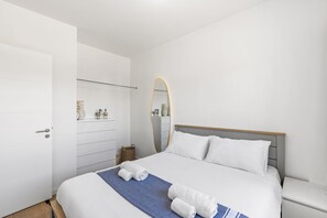 Et moderne soveværelse med en pænt redt seng, et sengebord, et spejl og et garderobeskab.