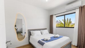 Ein modernes Hotelzimmer mit einem großen Bett, einem Spiegel, einem Fenster mit Vorhängen und einer Klimaanlage.