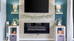 A modern living room with a flat-screen TV mounted above a fireplace, flanked by two wall-mounted lamps and shelves with decorative items. - Serene on Seventeen - For 4 (Branson)