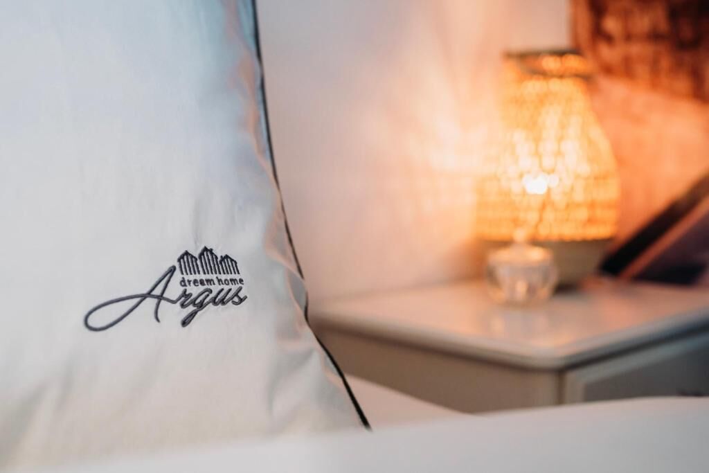 Un oreiller orné d’un logo et d’un texte, une table de chevet avec une lampe, et un arrière-plan flou.