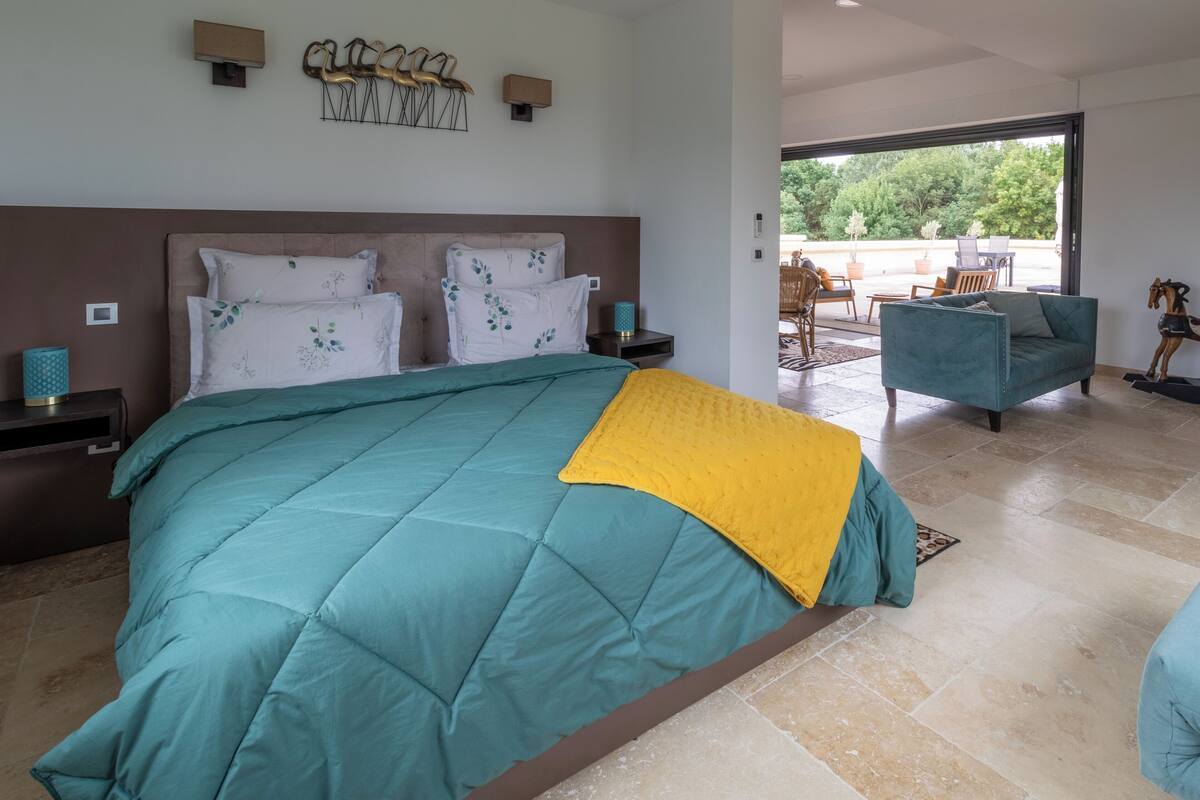 A bedroom with a large bed, a sofa, and a view of the outdoors.