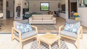 Un salon moderne comprenant un canapé, deux fauteuils, une table basse et donnant sur une chambre avec un lit et une fenêtre.