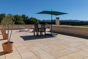 Une terrasse extérieure avec une table et des chaises, un parasol vert et des plantes en pot.