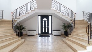 Une entrée imposante, avec une porte centrale, flanquée de deux escaliers dotés de rampes en métal et agrémentée de plantes en pot.
