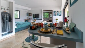 Une chambre d’hôtel moderne dotée d’un coin repas, d’un lit recouvert d’une couverture verte, d’une télévision et offrant une vue sur l’extérieur.