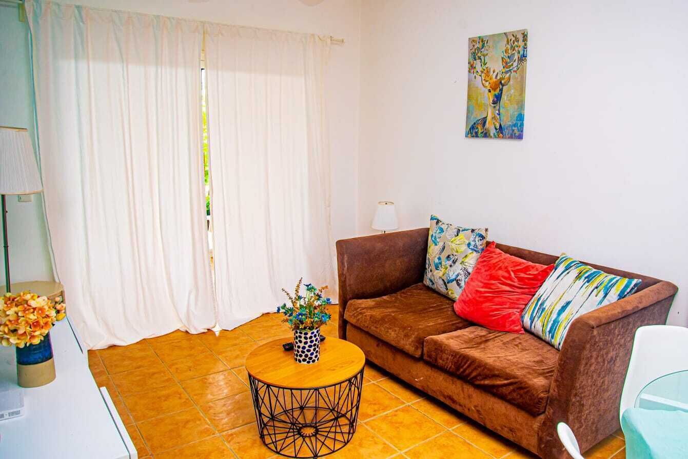 A living room with a brown sofa, colorful pillows, a round coffee table, and a painting on the wall.