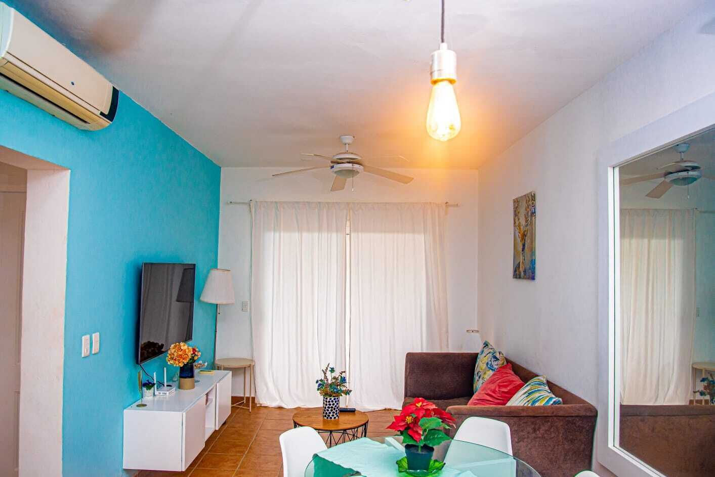 Una sala moderna con ventilador de techo, un comedor con mesa y sillas, y un sofá con cojines.