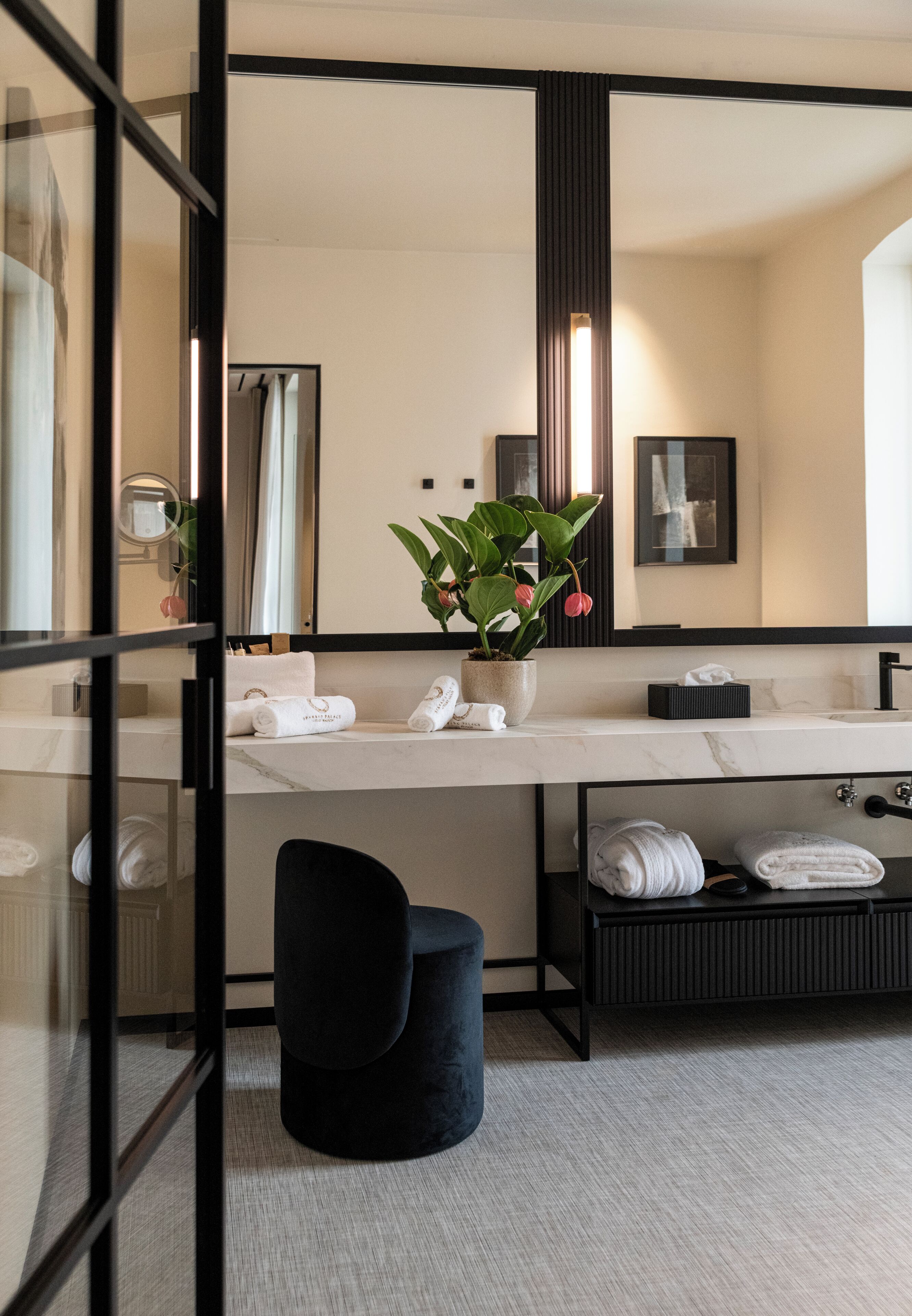 Un baño moderno con un espejo grande, un lavabo, una planta en maceta y toallas dobladas con cuidado.