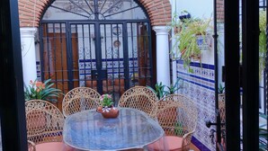 Eine Terrasse im Freien mit einem runden Tisch, Korbstühlen, gefliestem Boden und einem Zierbogen.