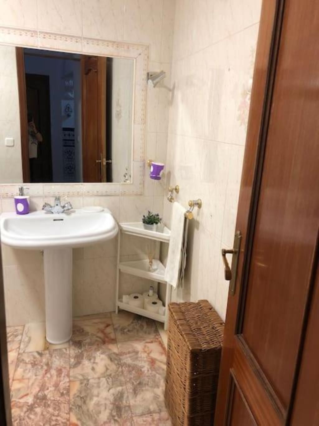 Un baño con lavamanos pedestal, un espejo, un perchero y una cesta de mimbre.