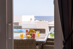 Una mesa de comedor con fruteros, bebidas y vistas al océano.